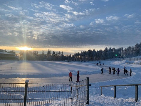 Joutsenon urheilukeskus talvella, luistelurinki kiertää kenttää ja luistelijat kuntoilevat auringossa